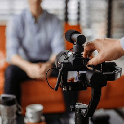 How corporate visuals can improve recruiting and hr initiatives 2 A hand holding a camera with person sitting on a couch in the background, representing corporate visuals