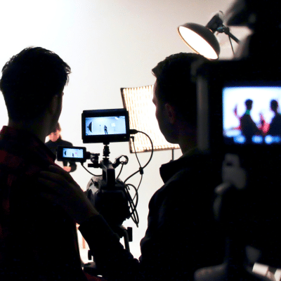 Your corporate media checklist: planning a corporate shoot that delivers results 2 Silhouettes of two camera men standing beside cameras and screens, getting ready for a shoot, representing planning a corporate shoot